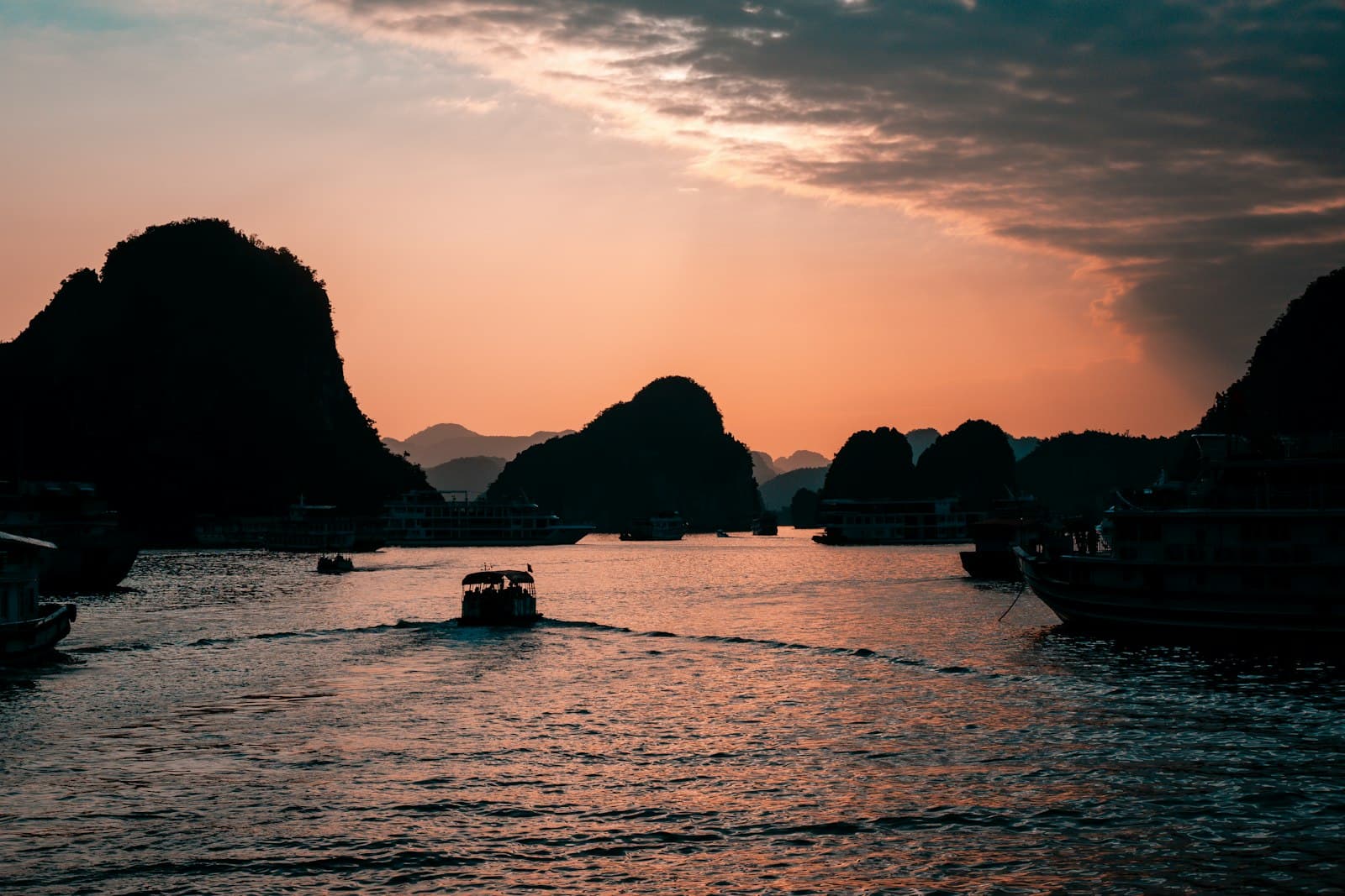 Tour boats crossing the limestone karsts of Ha Long Bay at sunset