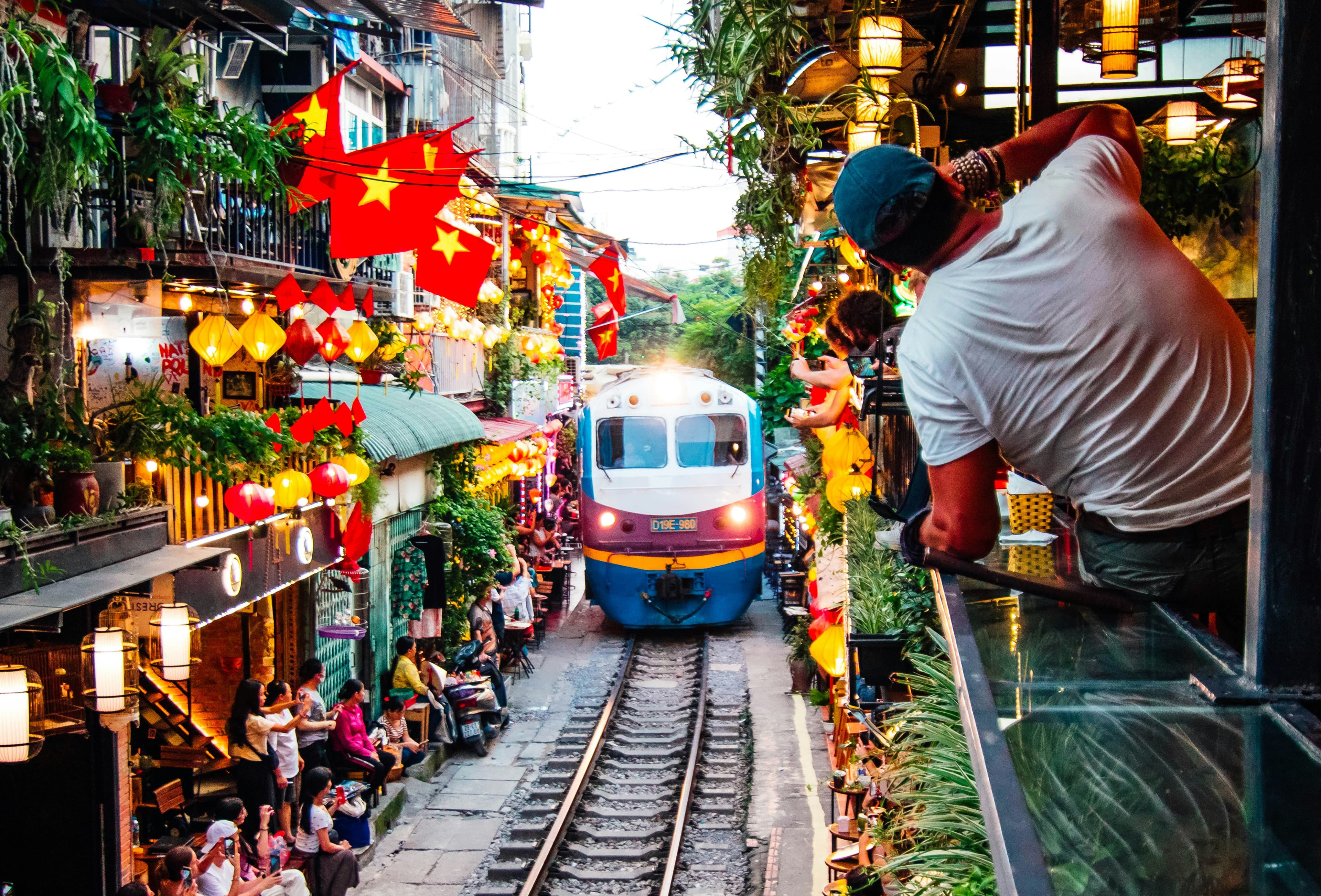 The Reunification Express easing through Hanoi's Train Street beneath strings of red flags